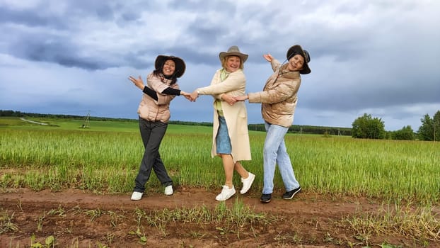 Adult girls looking like a cowboys in hats in a field and with a stormy sky with clouds posing in the rain. Women having fun outdoors on rural and rustic nature