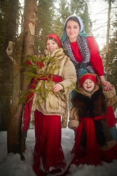 Family with mother, teenage girl, and little daughter dressed in stylized medieval peasant clothing in winter forest. Woman and her daughters pose for fairytale photoshoot in nature on a cold day