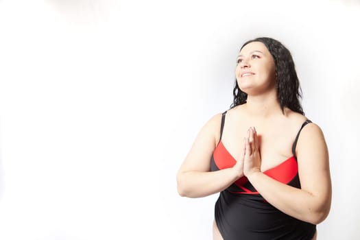 Portrait of attractive dreamy thick woman in red black swimsuit posing on white background. Body positive, photoshoot, selfie. Funny plus size model