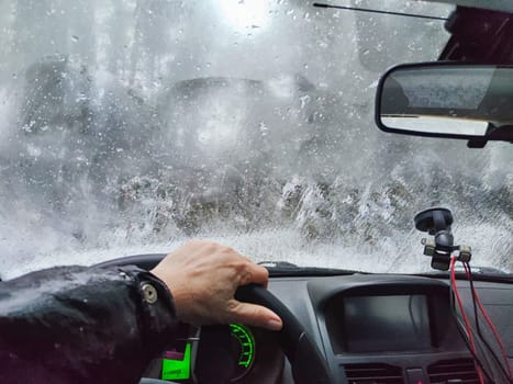 Hand of woman on steering wheel in car and and forest with cloudy windshield, fogged with snow ice in winter. Blurred woman driving car in travel