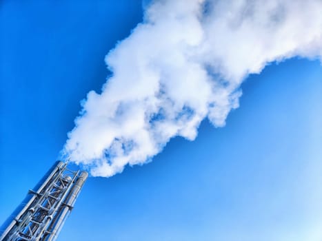 Air pollution by smoke coming out of two factory chimneys. White clouds of smoke against a blue sky background