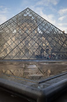 France, Paris - Jan 03, 2024 - At the front of Famous Louvre Museum and its grand glass pyramid during day time with water reflection effect by after raining. is one of the world's largest museums in Paris, Space for text, Selective focus.