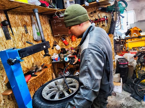 Ishim, Russia - November 27, 2023: Mechanic repairs a car wheel and makes a tire in a dirty garage. Replacement of summer wheels, tires for winter indoors