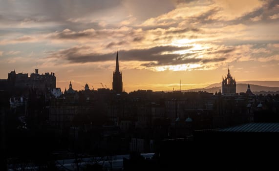 Evening sunset over view the castle downtown and old town district of Edinburgh City. Edinburgh city skyline buildings form silhouette shapes against the sky yellow background  at sunset, Destinations in Europe, Space for text, Selective focus.