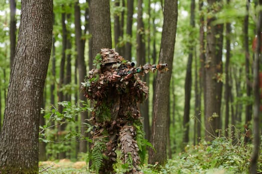 A highly skilled elite sniper, camouflaged in the dense forest, stealthily maneuvers through dangerous woodland terrain on a covert and precise mission.