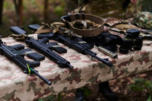An array of military weapons, including rifles and pistols, is meticulously arranged on a table in a military base, presenting a close-up view of the diverse firepower and armament meticulously organized for readiness and strategic deployment.
