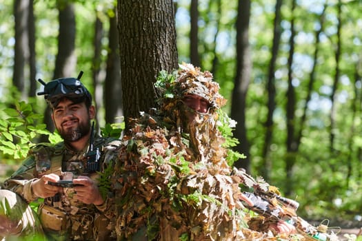 A skilled sniper and a soldier operating a drone with VR goggles strategize and observe the military action while concealed in the forest.