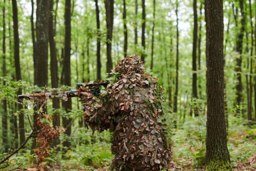 A highly skilled elite sniper, camouflaged in the dense forest, stealthily maneuvers through dangerous woodland terrain on a covert and precise mission.