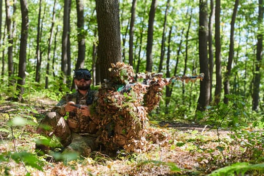 A skilled sniper and a soldier operating a drone with VR goggles strategize and observe the military action while concealed in the forest.