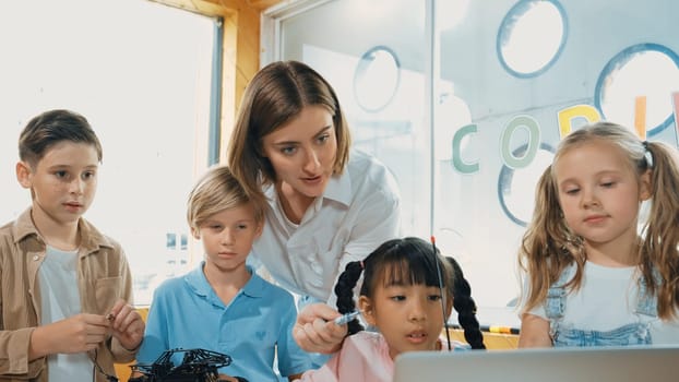 Smart teacher and diverse student looking at laptop on table with car model placed. Caucasian mentor inspect, explain, teaching engineering code or prompt in STEM technology classroom. Erudition.