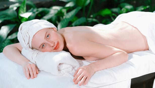 A beautiful young woman lies on a spa bed while looking at camera. Feeling of relaxed and at peace. Attractive caucasian woman surrounded by the calming sounds of nature. Tranquility