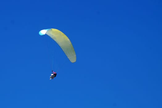 two people on a parachute wing with a clear blue sky, copy space.