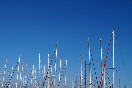 Yacht masts without sails against the background of a clear blue sky, copy space.