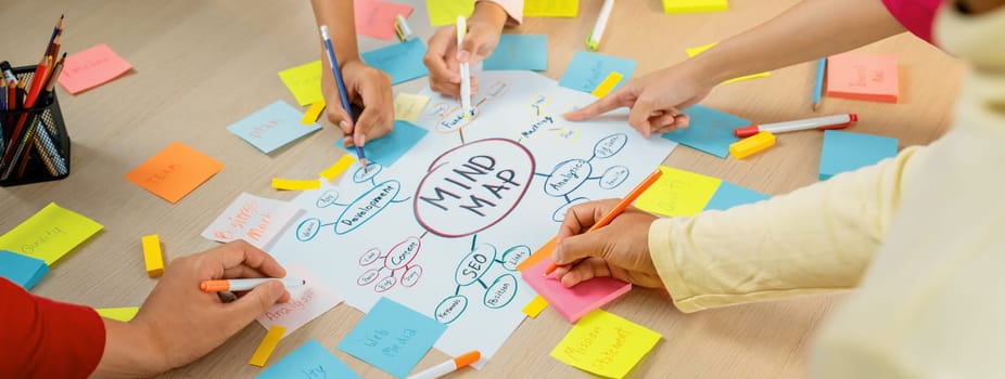 Professional startup group share creative marketing idea by using mind map. Young skilled business people brainstorm business plan while writing sticky notes. Focus on hand. Closeup. Variegated.