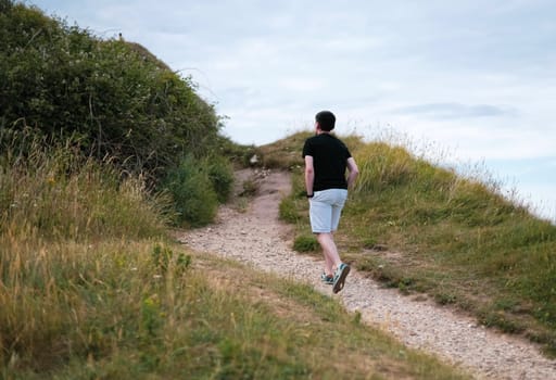 One young caucasian brunette guy in a black T-shirt and light shorts climbs on foot on a mountain top on a cloudy day admiring the view of the northern sea, side view close-up.