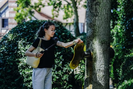 Portrait of one beautiful Caucasian brunette teenage girl with a mini camera on a stick turns a large golden key sticking out of a tree trunk on a sunny summer day, close-up side view.