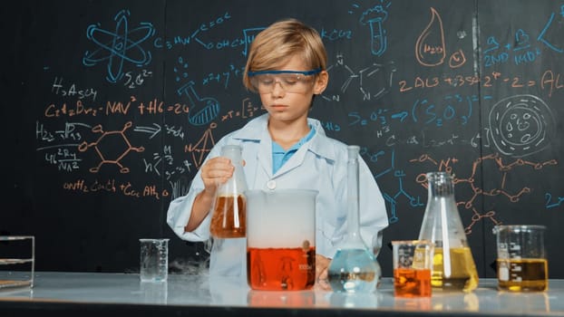 Smart boy inspect mixed chemical liquid in laboratory beakers while holding and looking carefully. Caucasian child focus on doing an experiment in chemistry lesson or STEM science class. Erudition.