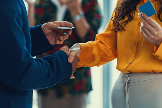 Businessmen shaking hand and making a contract in the sign of agreement, cooperation with businesswoman. Cropped image of managers holding business cards. Their partners standing behind. Intellectual.