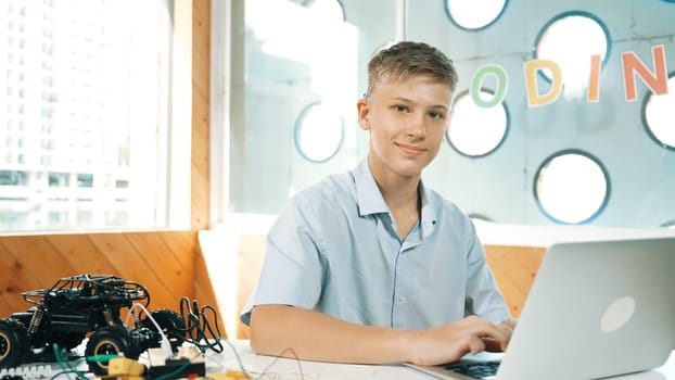 Teenager working on laptop and looking at camera at STEM technology class. Caucasian highschool student using computer to analyze data while looking at camera on table with car model. Edification.