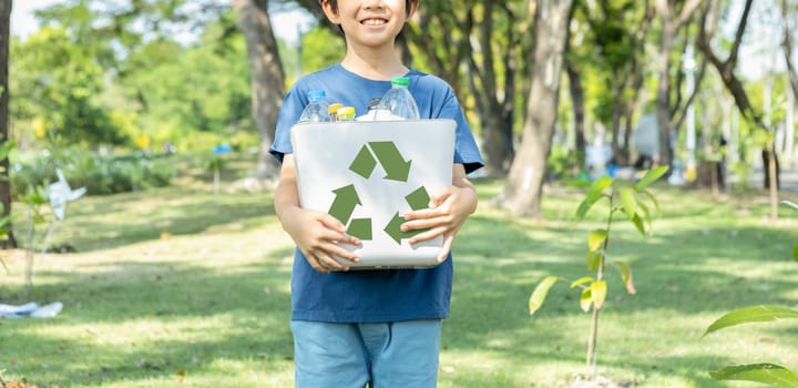 Cheerful young asian boy holding recycle symbol bin on daylight natural green park promoting waste recycle, reduce, and reuse encouragement for eco sustainable awareness for future generation. Gyre