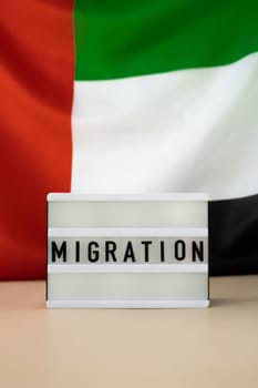 Message MIGRATION on background of UAE flag made from silk. United Arab Emirates national flag with concept of tourism and traveling. Dubai welcoming card. Advertisement