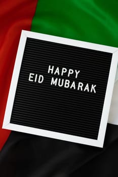 Congratulations with text HAPPY EID MUBARAK - happy holidays waving UAE flag on background concept. Greeting card advertisement. Commemoration Day Muslim Ramadan Blessed holy month public holiday. Patriotism