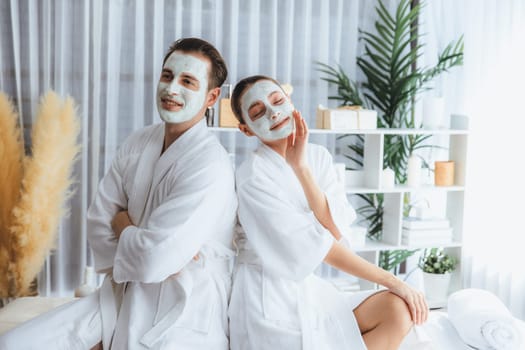 Blissful couple in bathrobe with facial cream mask enjoying serene ambiance of spa salon resort or hotel during holiday. Pampering face spa and skincare treatment with essence relaxation. Quiescent