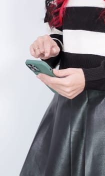 Teenager girl in a white and black sweater and leather skirt is using smart phone. Faceless, vertical. Social media, music, testing, online shopping