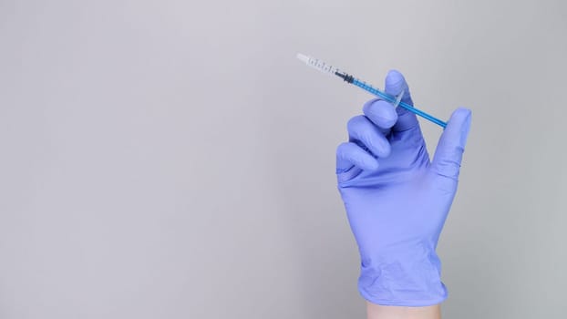 Hand in blue gloves of doctor or nurse holding syringe with liquid vaccine over grey background with copy space. New vaccine. Unknown vaccine. Medical gloves