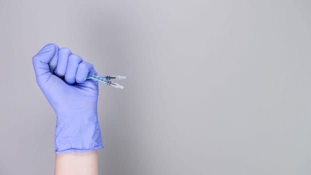 Hand in blue gloves of doctor or nurse holding syringe with liquid vaccine over grey background with copy space. New vaccine. Unknown vaccine. Medical gloves