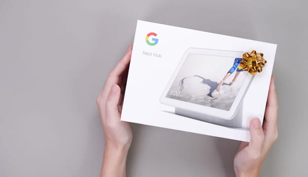 Hands holding gift box of Google Nest Hub on the grey background. Christmas gift. Space for text. Gatineau, QC Canada - Dec 21, 2022