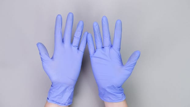 Hands in blue gloves of doctor or nurse over grey background with copy space. Medical gloves