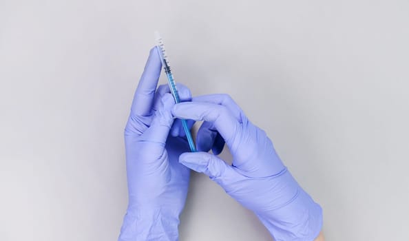 Hands in blue gloves of doctor or nurse holding syringe with liquid vaccine over grey background with copy space. New vaccine. Unknown vaccine. Medical gloves