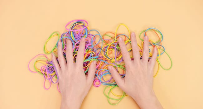 Hands hiding colored rubber bands for money on bright yellow paper background. Abstract background. Stationery accessories