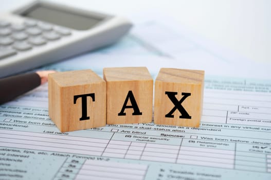 Tax wordings on wooden cubes with tax form and calculator background. Taxation concept.