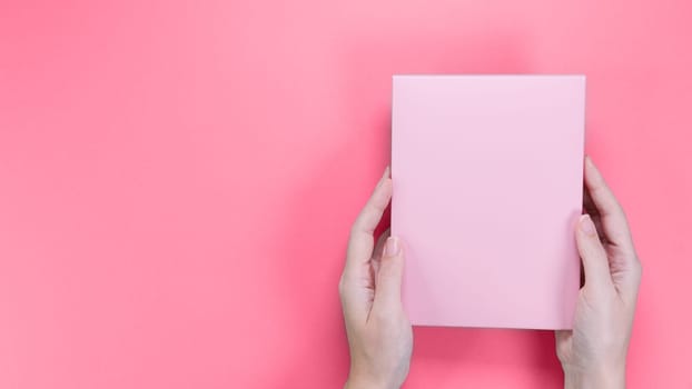 A square pink box with an copy empty space for text and design in hand of young woman in on a pink background. Color of year 2023 Viva Magenta. Board, blank, template, mockup, layout for a slogan