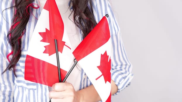 Unrecognized girl student in white blue shirt holding small canadian flag over gray background, Canada day, holiday, vote, immigration, tax, copy space.