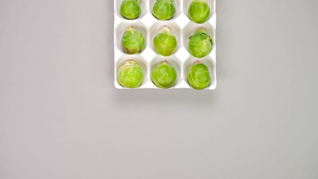 Raw organic Brussel sprouts in yellow white egg container on grey background, top view. Flat lay, overhead, from above. Copy space.