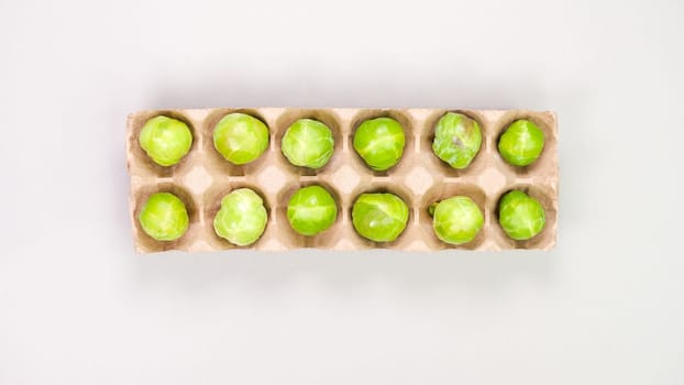 Raw organic Brussel sprouts in brown egg container on grey background, top view. Flat lay, overhead, from above. Copy space