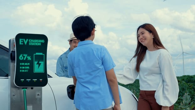 Modern family travel and nature with eco-friendly EV car concept, recharging battery from charging station using renewable energy from wind turbine for future energy sustainability. Peruse