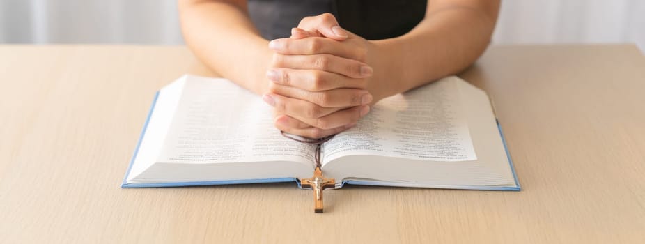 Cropped image of praying male hand holding cross on holy bible book at wooden table. Top view. Concept of hope, religion, faith, christianity and god blessing. Warm and brown background Burgeoning.