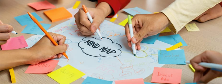 Professional startup group share creative marketing idea by using mind map. Young skilled business people brainstorm business plan while writing sticky notes. Focus on hand. Closeup. Variegated.