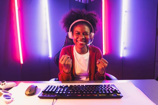 Gaming streamer, African girl playing online fighting with Esport skilled team wearing headphones in neon color lighting room. Talking other players planing strategies to win competitors. Tastemaker.