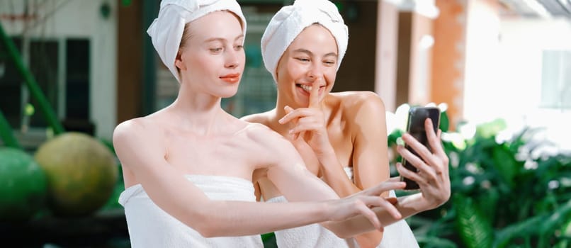 Couple of young beautiful women with beautiful skin in white towel taking a photo together at outdoor surrounded by peaceful natural environment. Beauty and healthy spa concept. Tranquility.