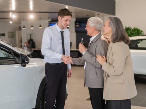 A salesman hands over the keys to a new car to an elderly Caucasian couple