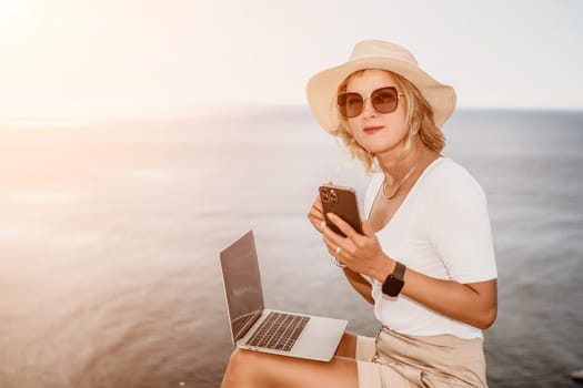 Digital nomad, Business woman working on laptop by the sea. Pretty lady typing on computer by the sea at sunset, makes a business transaction online from a distance. Freelance remote work on vacation