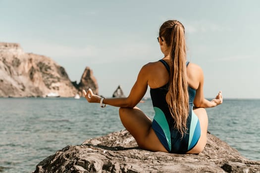 Yoga on the beach. A happy woman meditating in a yoga pose on the beach, surrounded by the ocean and rock mountains, promoting a healthy lifestyle outdoors in nature, and inspiring fitness concept