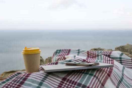 Laptop coffee on blanket with ocean view. Illustrating serene outdoor laptop use. Freelancer enjoying their time outdoors while working or browsing the internet