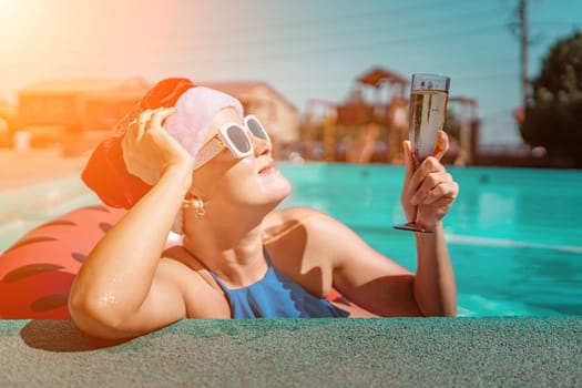 Woman pool Santa hat. A happy woman in a blue bikini, a red and white Santa hat and sunglasses poses near the pool with a glass of champagne standing nearby. Christmas holidays concept