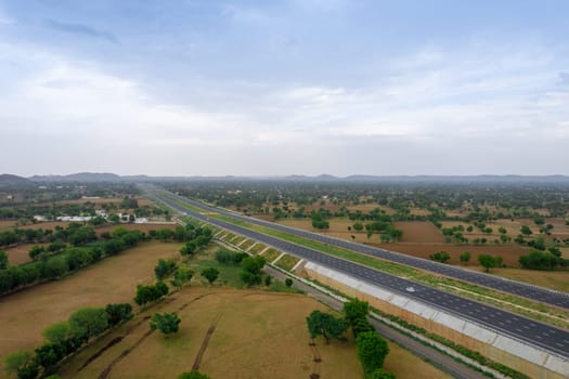 aerial drone rising over pond and green fields with delhi mumbai highway stretching off into distance with clouds tinted pink at dusk showing the beautiful landscape of India and travel